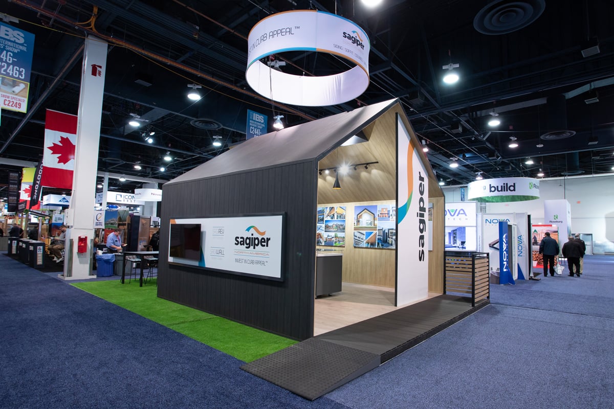 A custom trade show booth with a roof, two walls and a floor with lighting. The structure is surrounded with astroturf and has an accessible ramp.